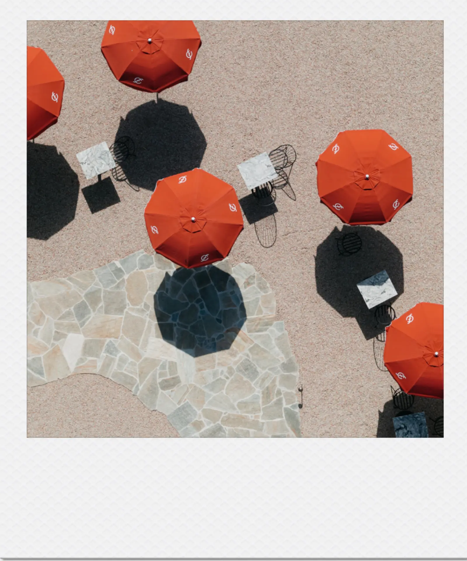 Overhead view of red umbrellas and shaded tables on a sunny terrace